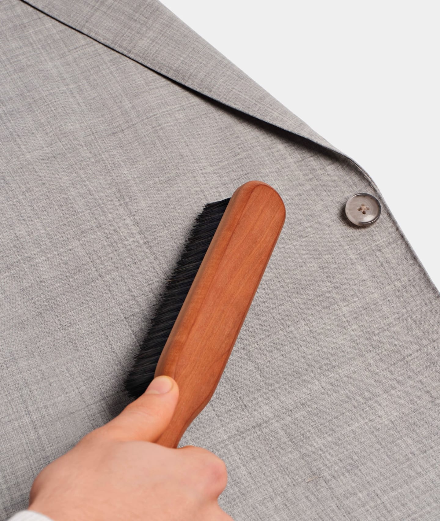 Brossage d'une veste de costume gris à l'aide d'une brosse en bois à soies de sanglier.