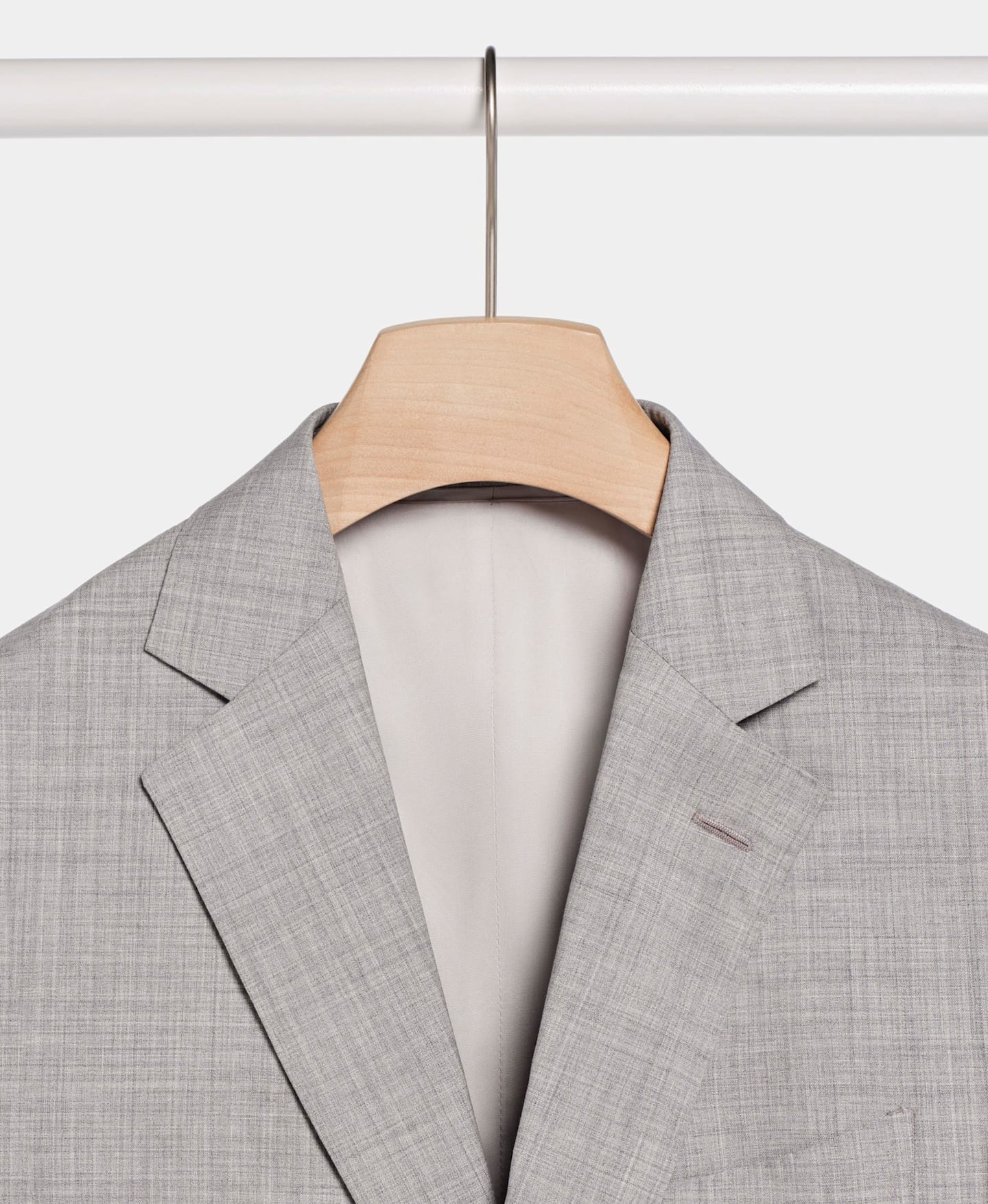 Imagen detallada de un blazer de traje gris claro colgado de una percha de madera
