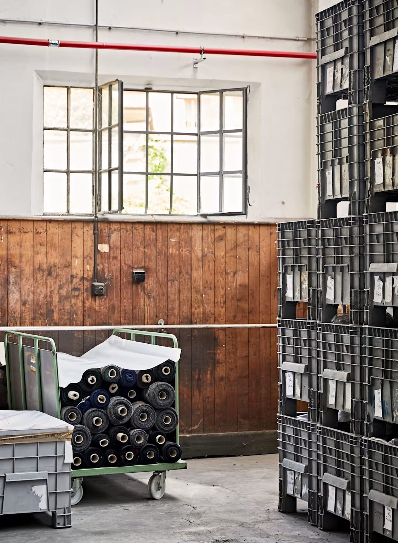 Fabric rolls stacked on a green metal cart in a warehouse with tall storage crates