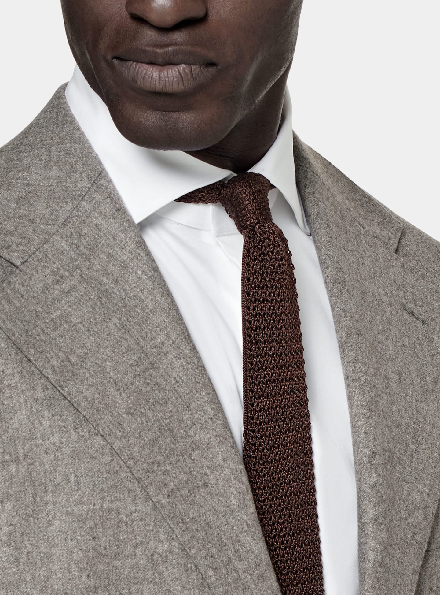 Dettaglio di abito monopetto grigio con cravatta marrone in seta lavorata a maglia.