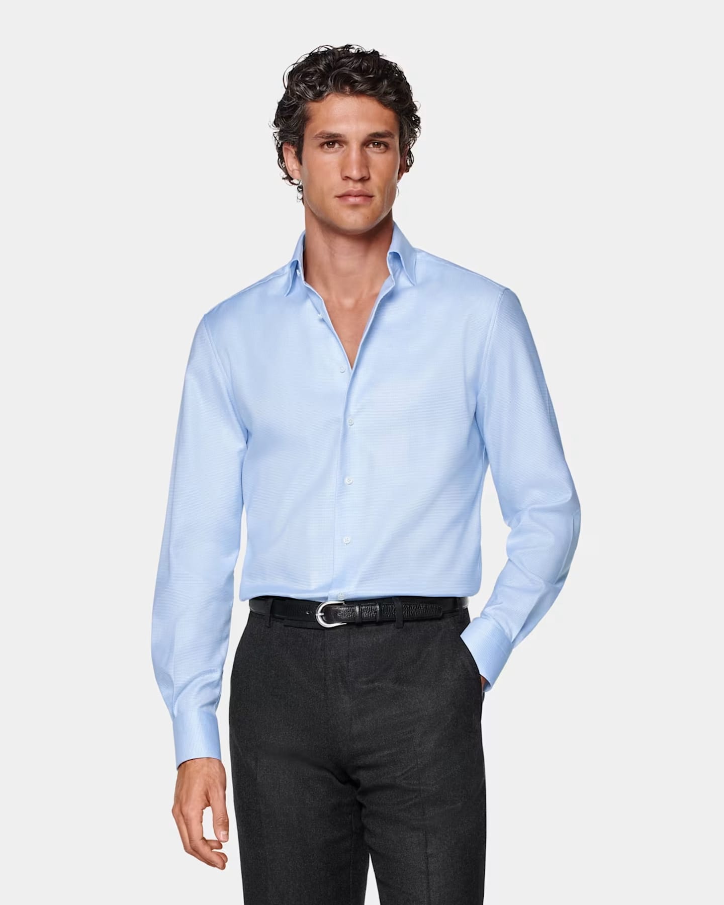 Wearing a blue shirt and black pants stands confidently, showcasing a casual yet polished appearance.