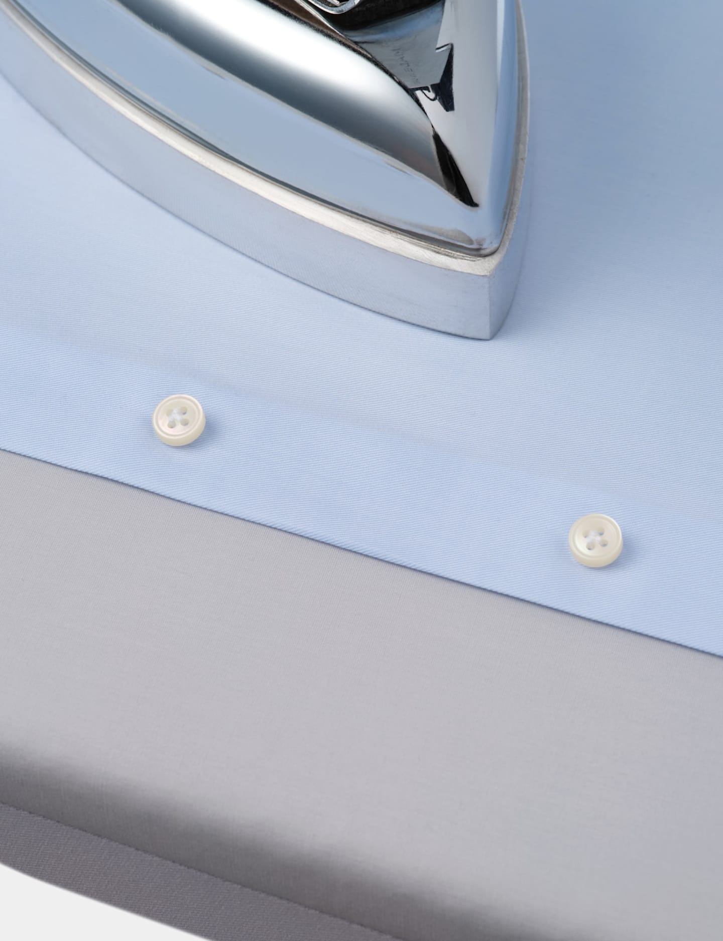 A close-up of a silver iron placed on a blue shirt, emphasizing the smooth surface of the iron against the shirt's color.