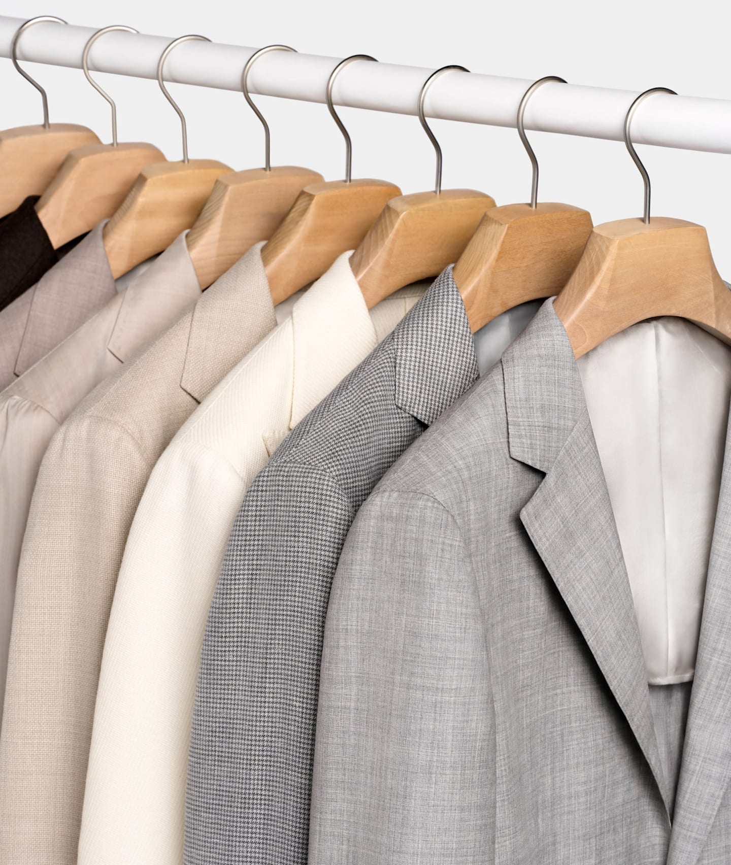 Stand appendiabiti dove sono appese delle giacche da abito grigio chiaro, a quadri e marrone chiaro.