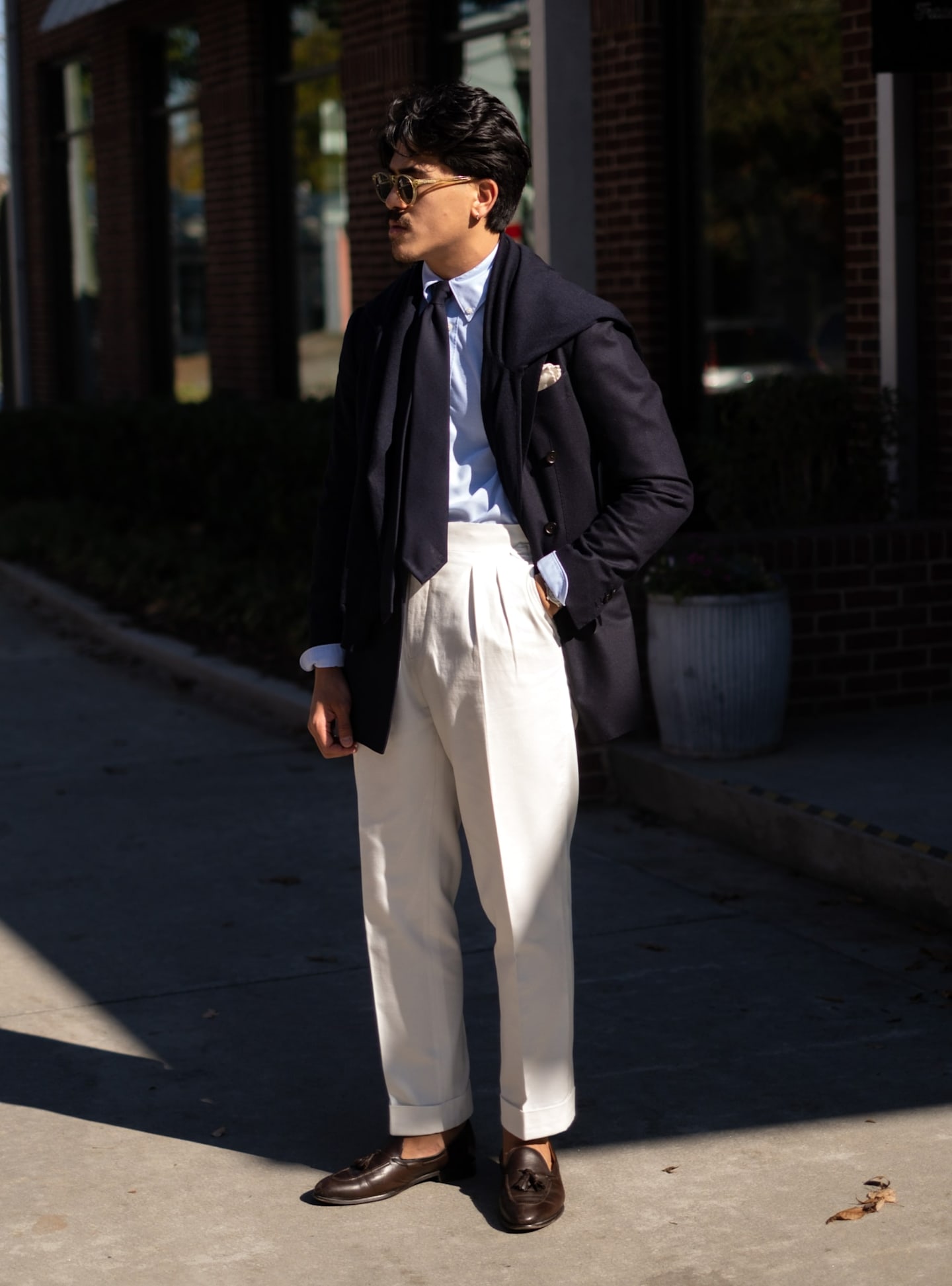 Double-pleated light brown trousers paired with navy blazer, light blue shirt, and navy tie.