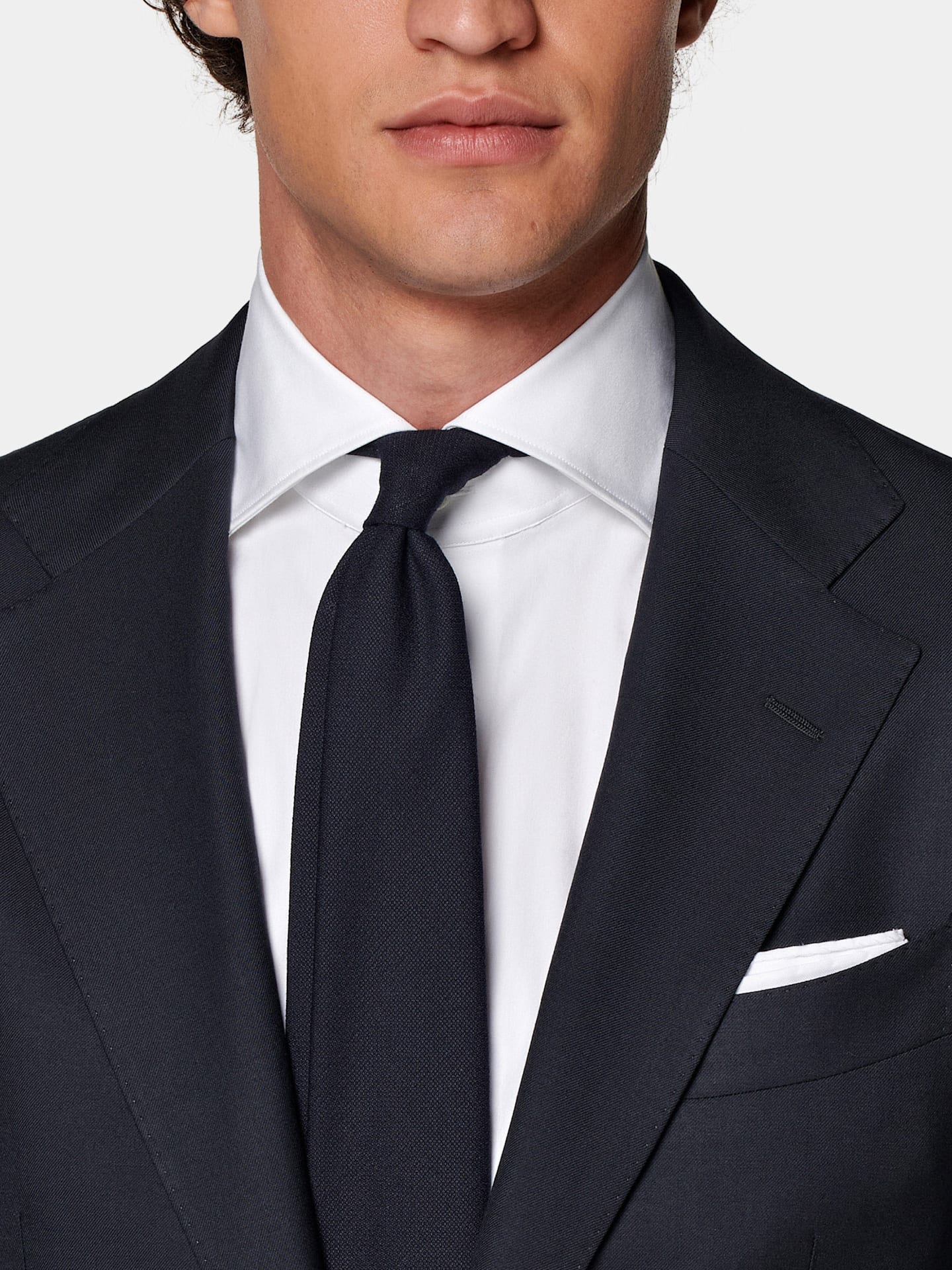 Detail of black two-piece suit with white shirt, black tie, and white pocket square.