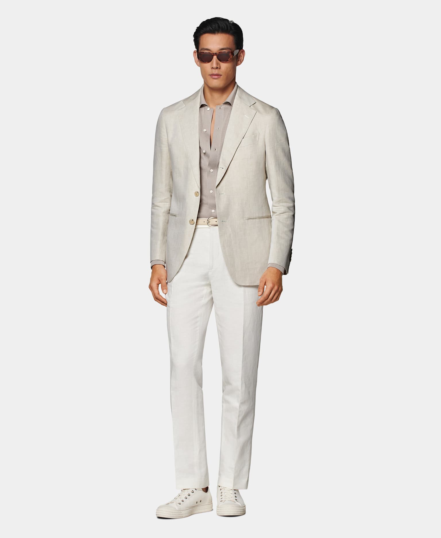 Blazer marrón claro con camisa gris topo, cinturón en tono tostado, pantalones blancos y sneakers de lona color crudo.