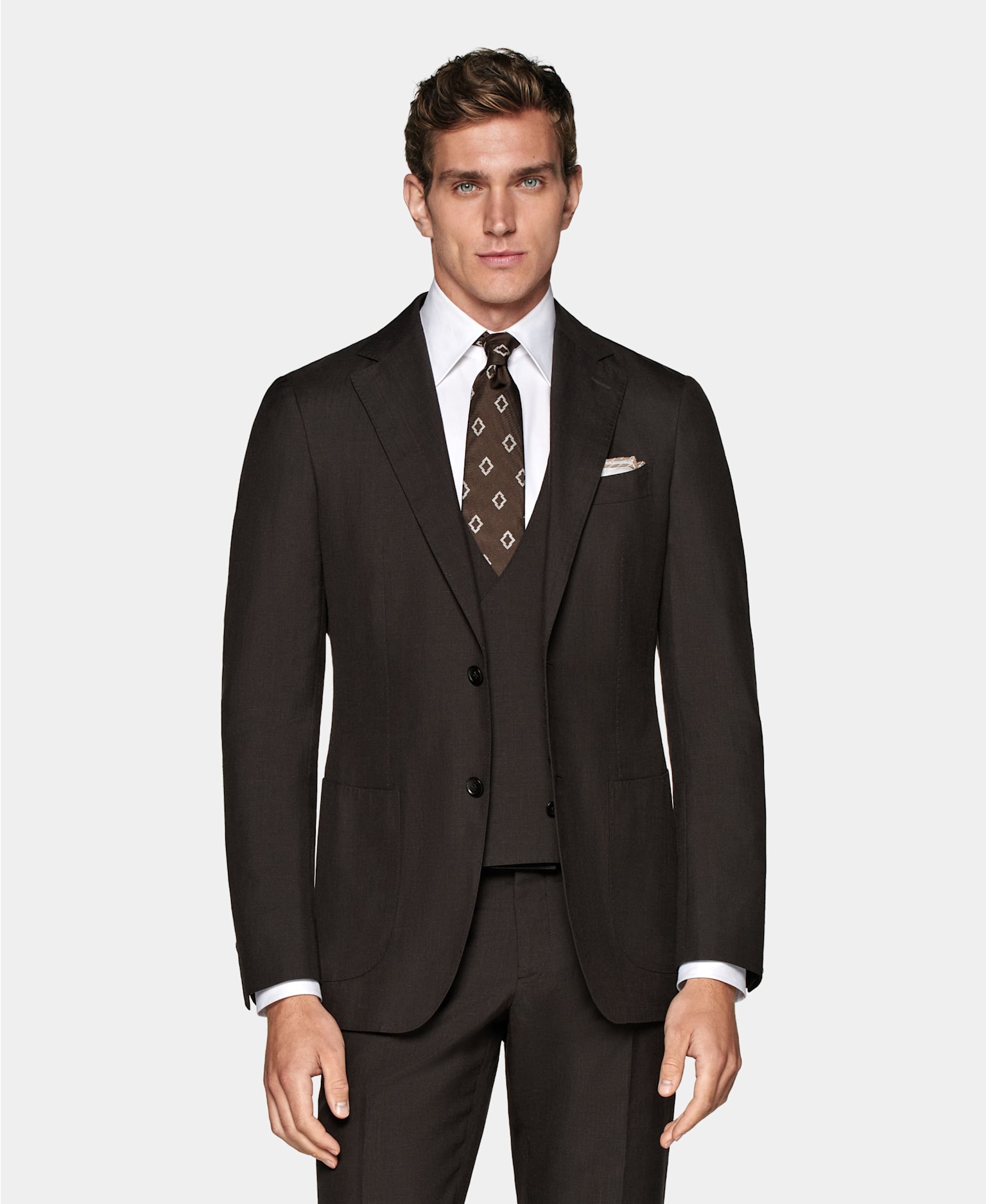 Ciemnobrązowy trzyczęściowy garnitur zestawiony z białą koszulą, brązowym krawatem we wzory i poszetką.