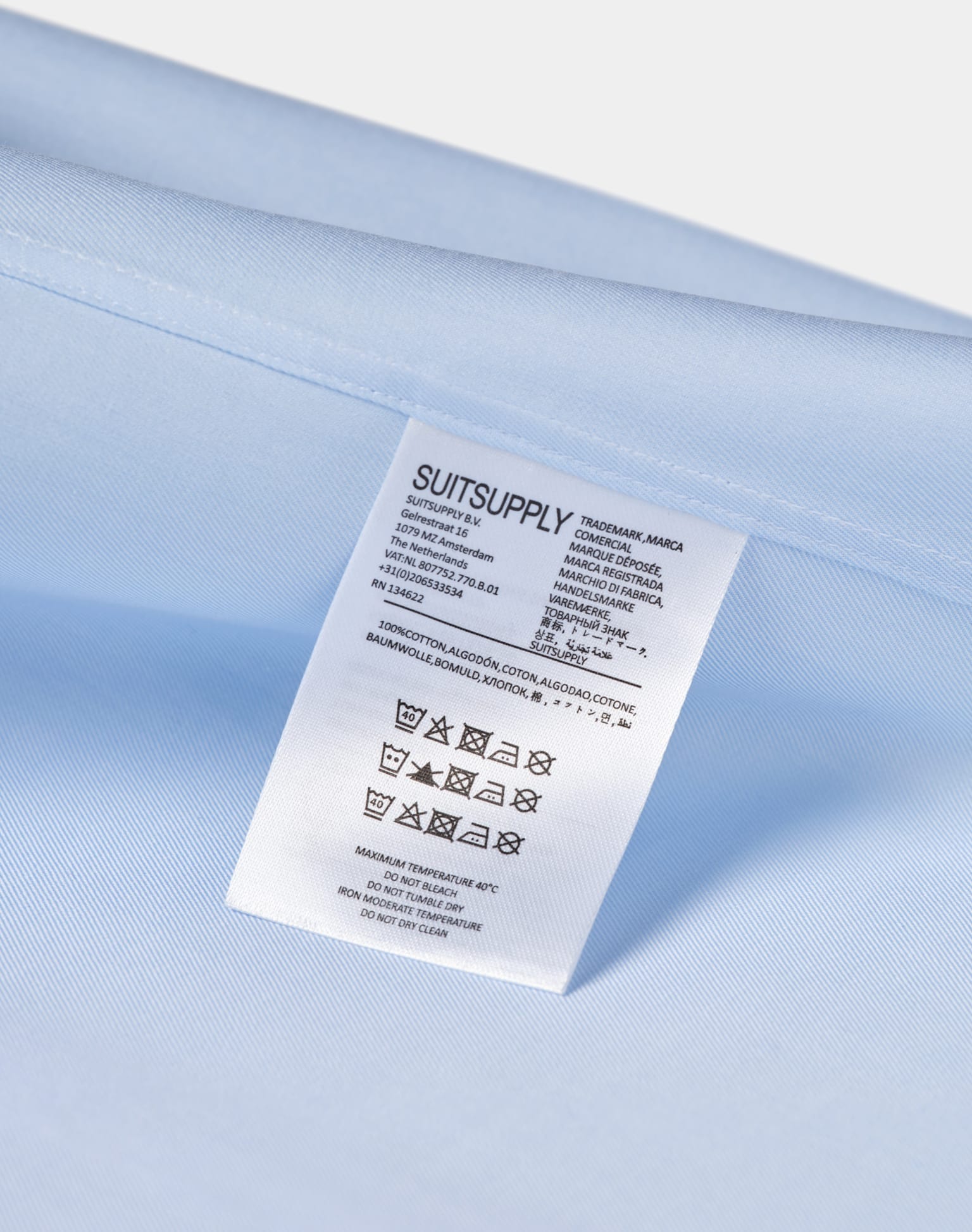 A close-up view of a white label stitched onto a light blue shirt fabric, showcasing the label's details and texture.
