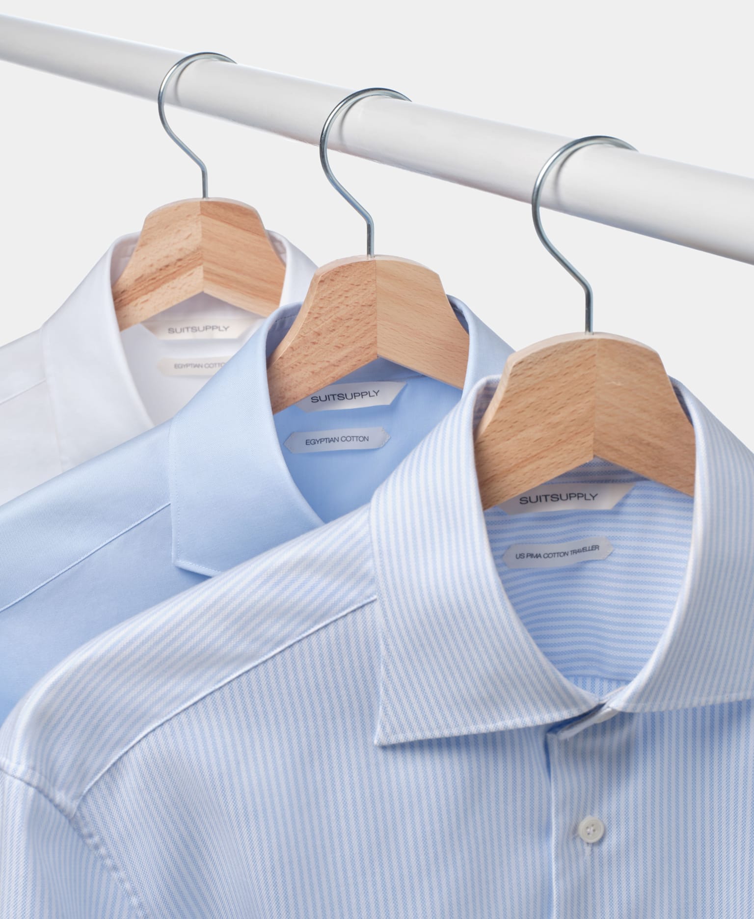 Three shirts of various colors neatly hanging on a clothes rail, showcasing their distinct styles and fabrics.