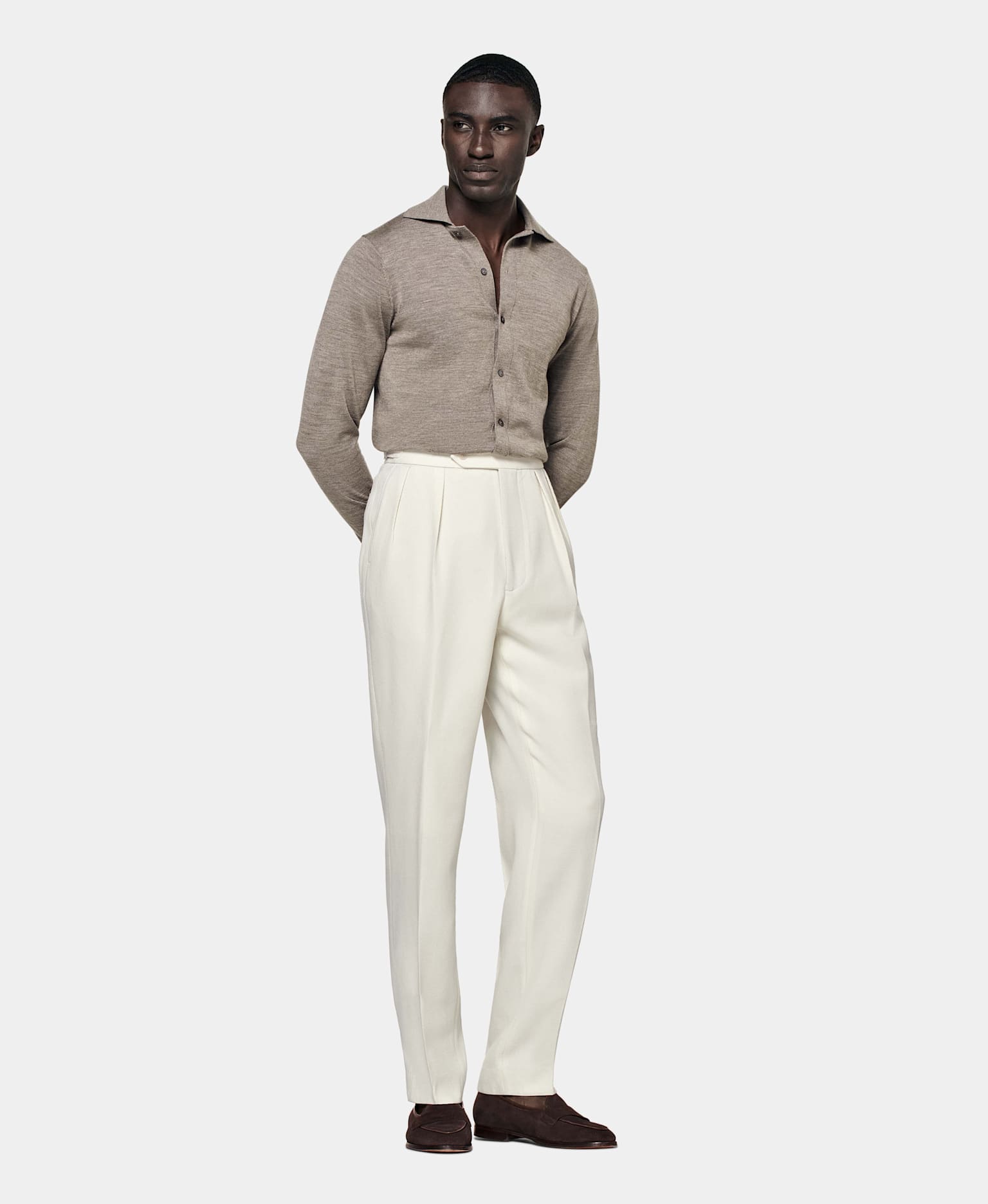 Double-pleated off-white trousers with tapered lower leg paired with brown knit and loafers.