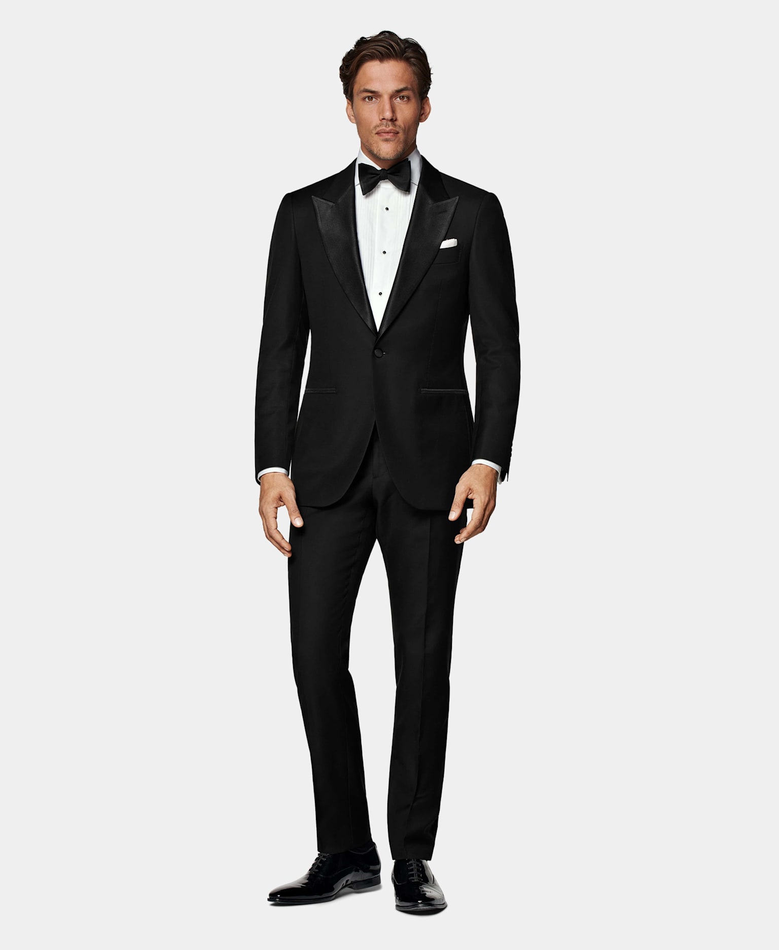 Black tuxedo with pleated white shirt, white pocket square, and black silk bow tie.