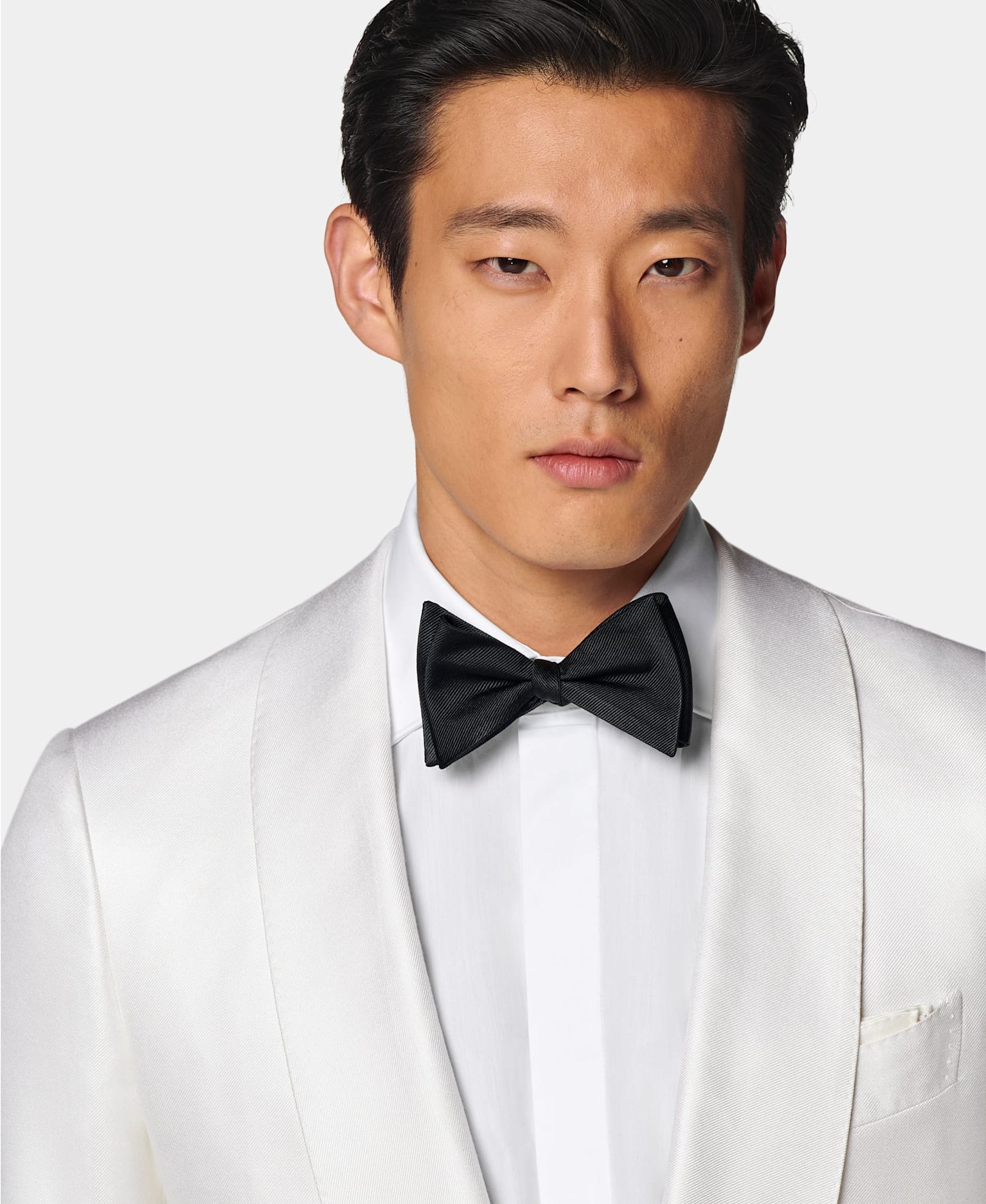 Vue de détail d'une veste de smoking blanche à col châle avec chemise blanche à gorge cachée et nœud papillon en soie noir.