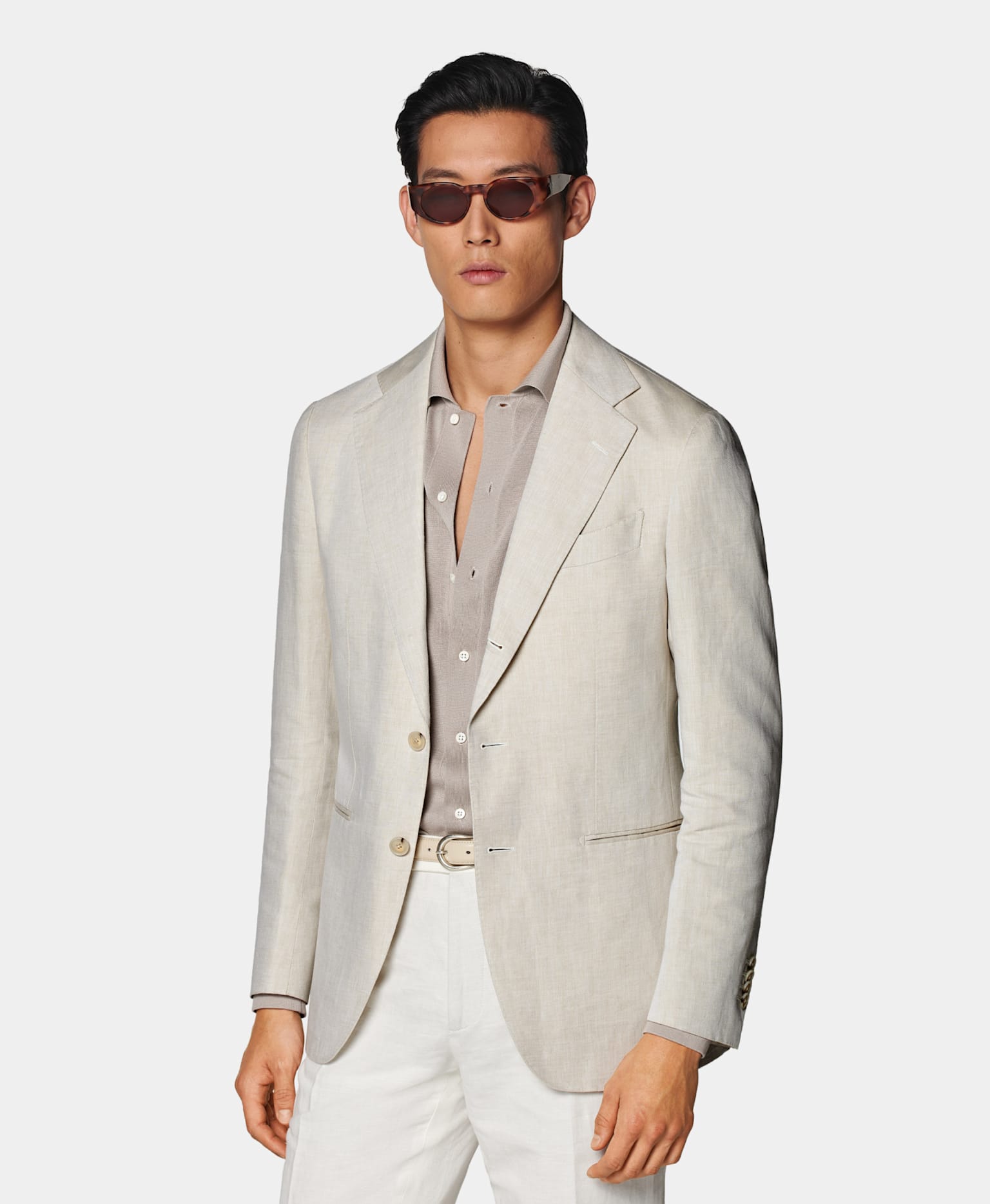 Blazer sable avec chemise en maille taupe, ceinture blanc cassé en cuir et pantalon blanc.